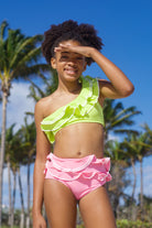 A child wearing a one-shoulder style yellow and pink bikini with a large ruffle and white ric-rac trim.